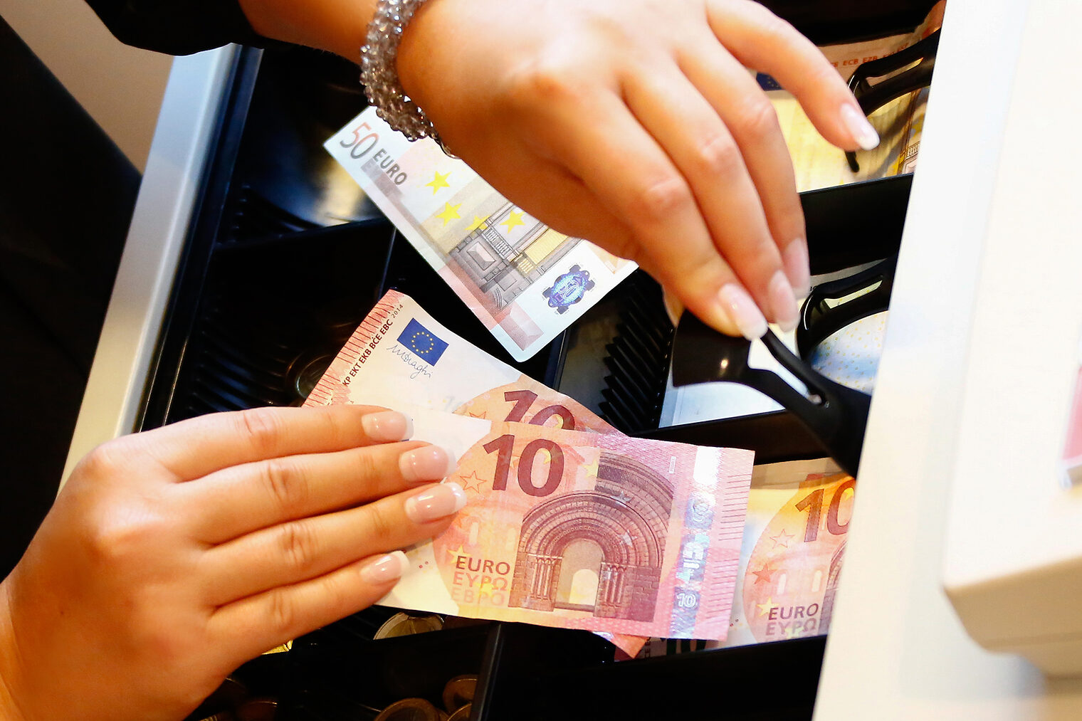 Nahaufnahme zweier Hände die Geld in eine Kasse einsortieren