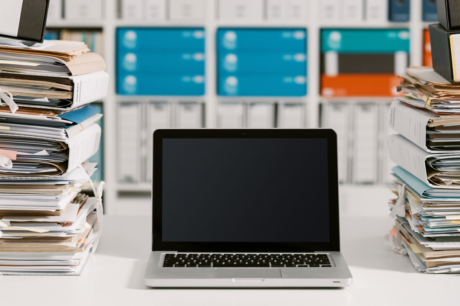 Laptop steht zwischen zwei Stapeln Akten