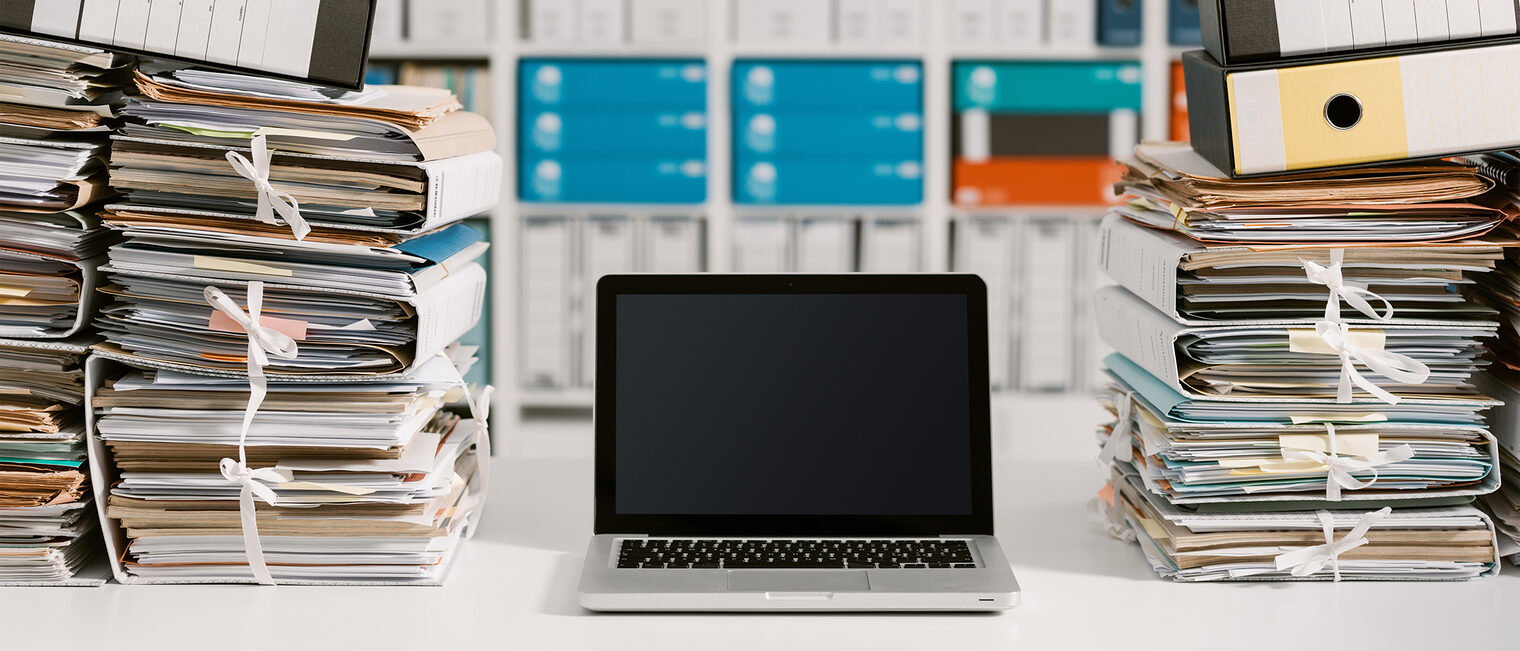 Laptop steht zwischen zwei Stapeln Akten