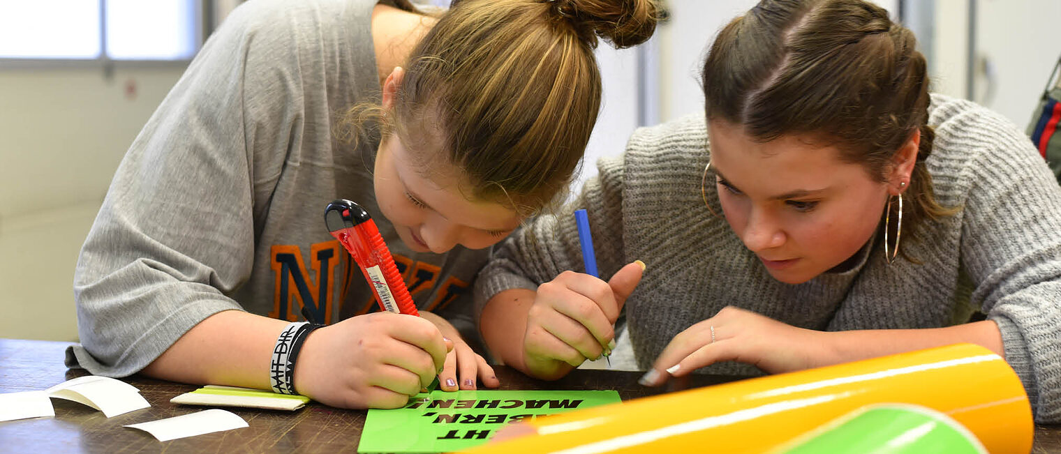 Zwei Mädchen arbeiten handwerklich am Berufsinformationstag Zwei Mädchen arbeiten an Schriftzug mit Cutter und Stift