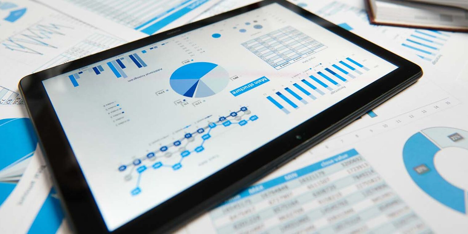 Tablet und Zettel mit Diagrammen und Zahlen auf einem Schreibtisch