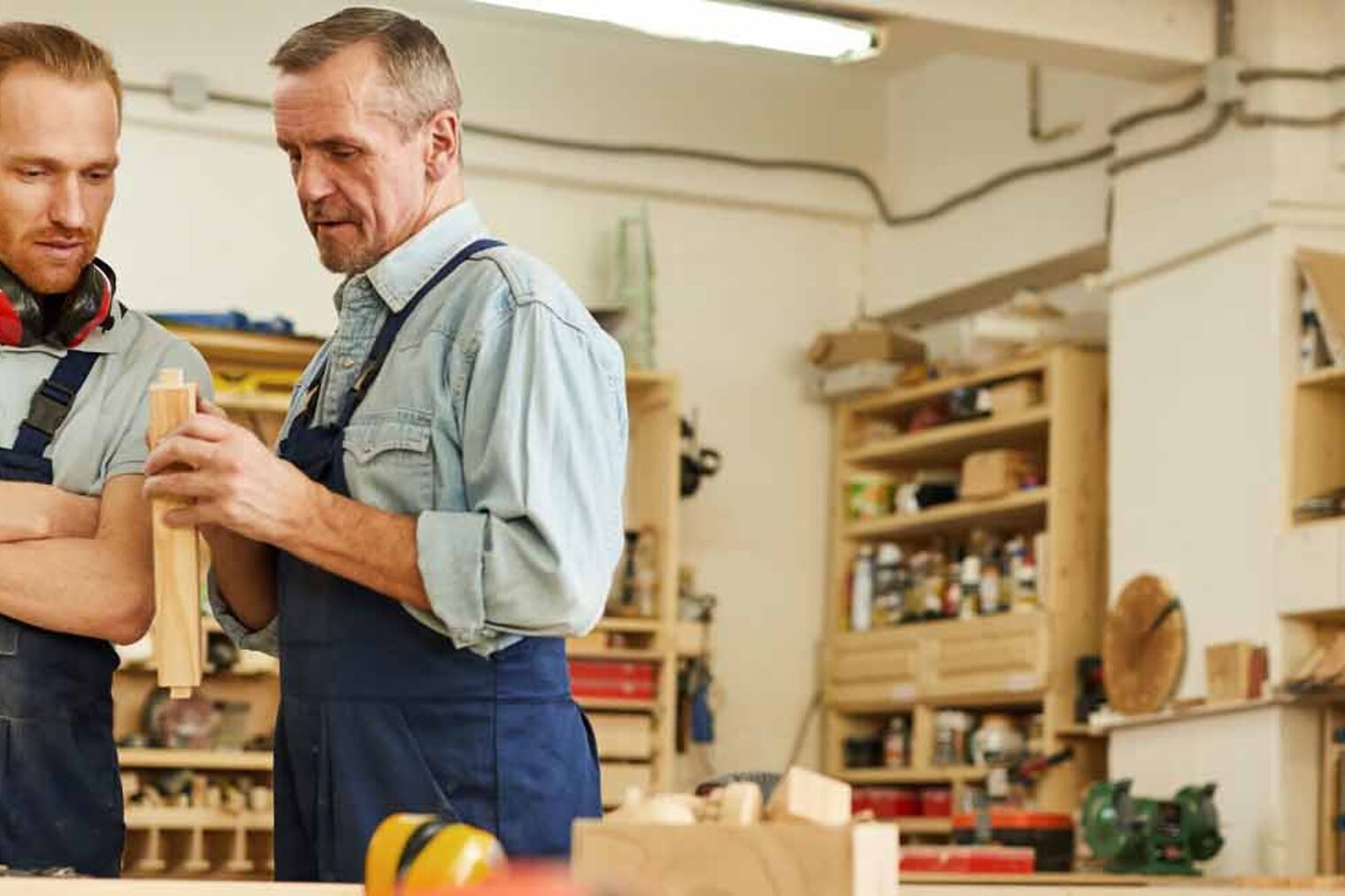 Unternehmensnachfolge Ein junger und ein älterer Handwerker stehen in einer Werkstatt und besprechen sich