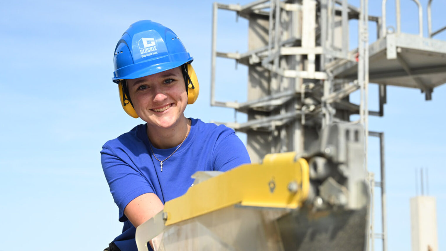 Maurerin auf Baustelle an einer Baumaschine, lächelt in Kamera