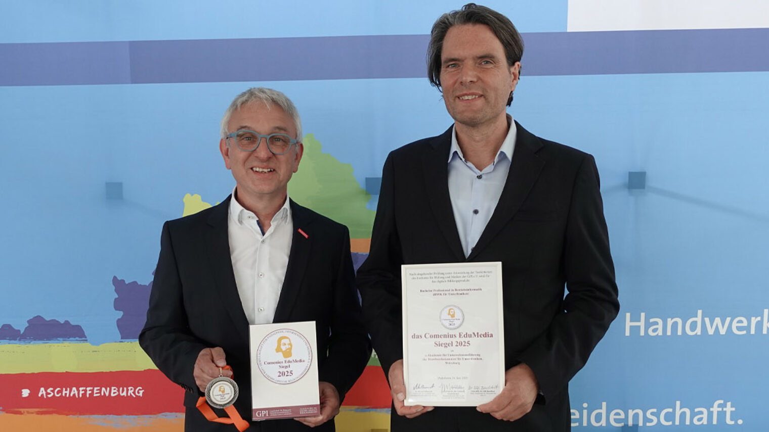 Foto zweier Personen, die Kamera blicken und Auszeichnung in den Händen halten