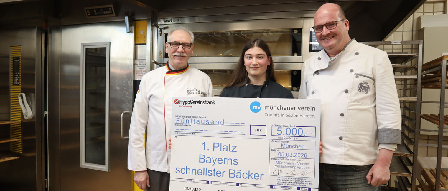 Drei Personen, in der Mitte Siegerin mit großem Symbolscheck