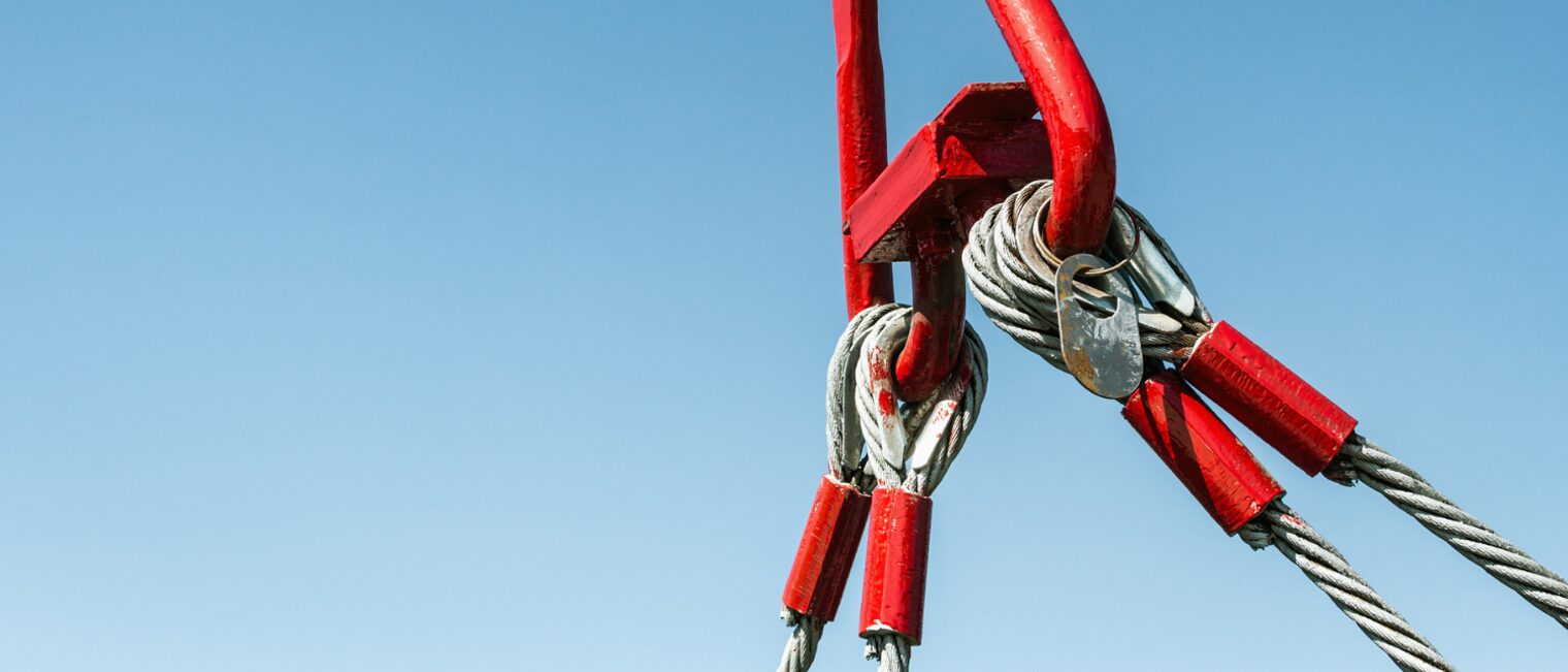 Symbolbild eines Stahlseils, das an einem roten Metallhaken befestigt ist