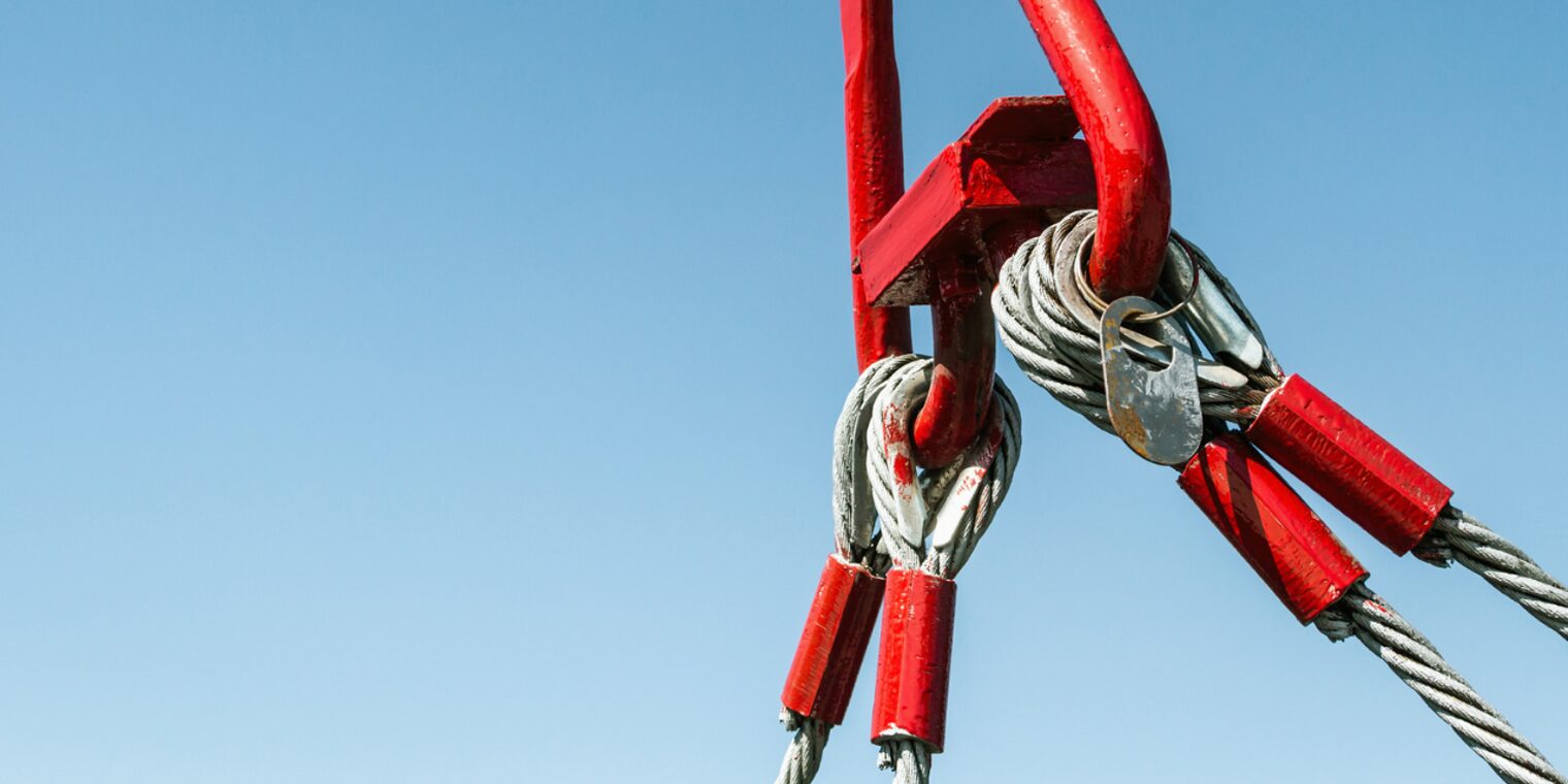 Symbolbild eines Stahlseils, das an einem roten Metallhaken befestigt ist