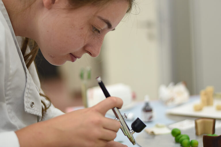 Mit einer Airbrush-Pistole trägt die Meisterschülerin Lebensmittelfarben auf ihre Marzipanfiguren auf.
