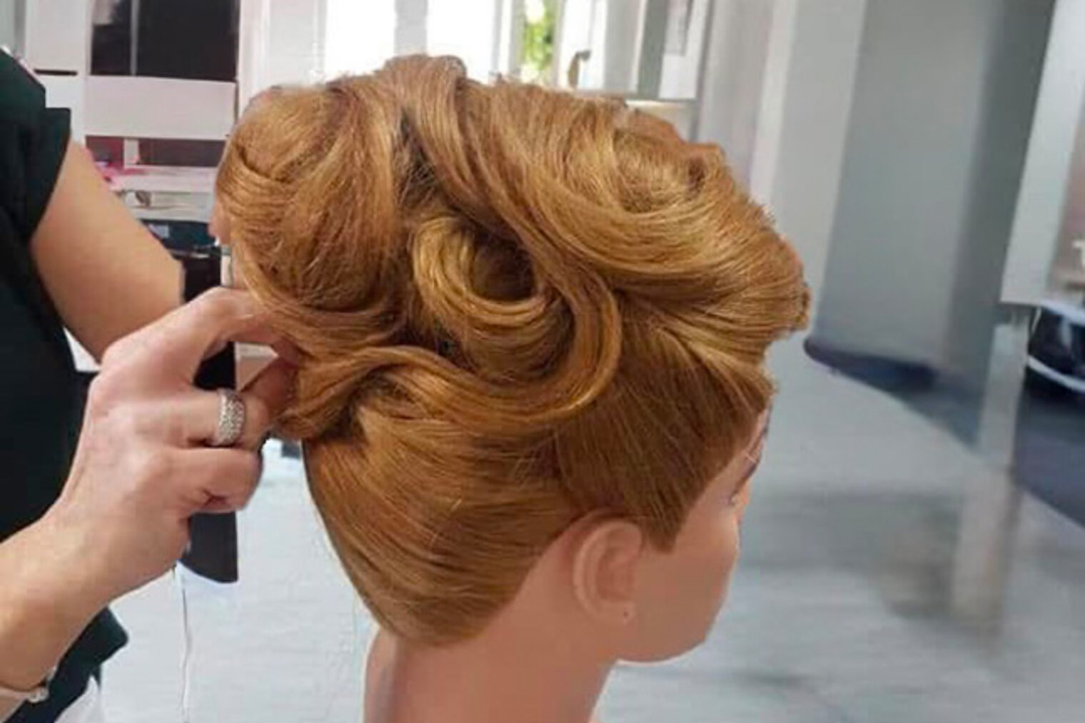Hände gestalten eine elegante Hochsteckfrisur am Übungskopf – Praxisübung für professionelle Stecktechniken