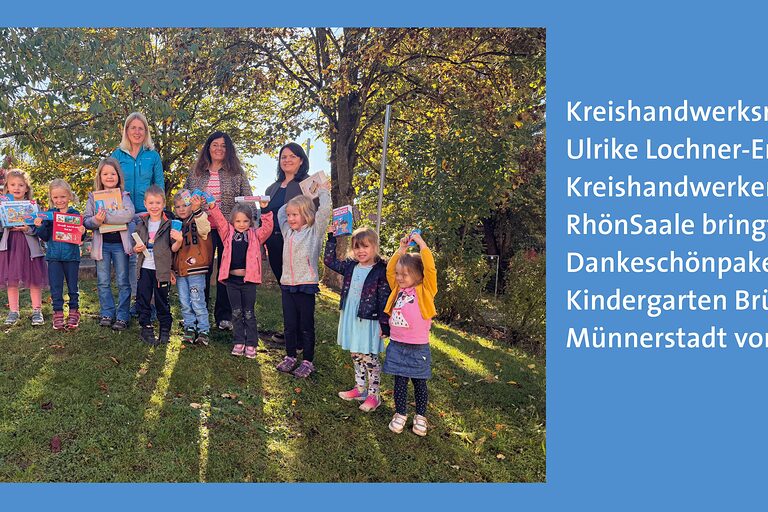 Gruppenbild im Garten, mehrere Kindergartenkinder halten Spielsachen hoch und lachende Erwachsene stehen im Hindergrund.